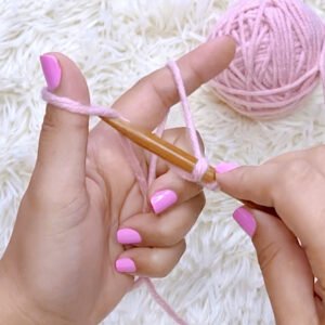 Mãos montando o ponto na agulha de tricô com fio rosa